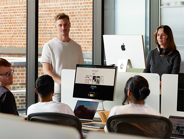 Cinco personas de Apple reunidas en torno a sus mesas, hablando.