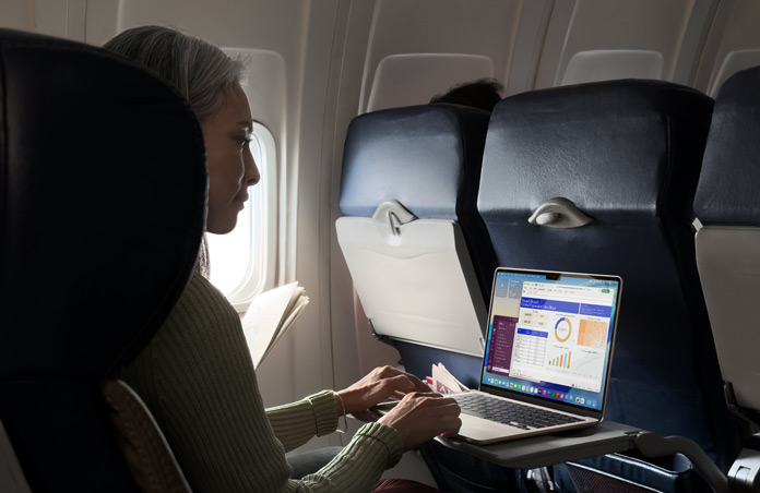 A person working on their MacBook Air while in an aeroplane seat