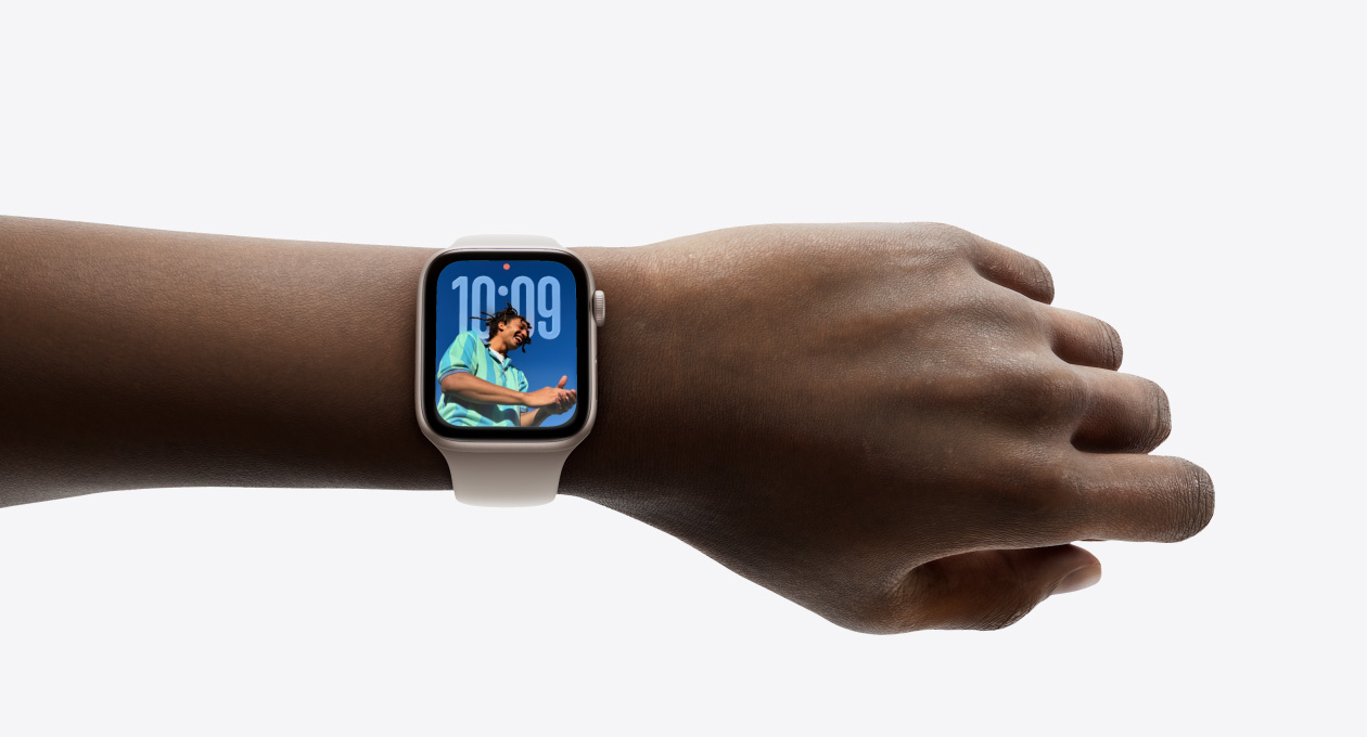 Nærbillede af rosaguld Apple Watch med gummiurrem på et håndled. Skærmen viser Tid-appen i det nye Liquid Glass-design.