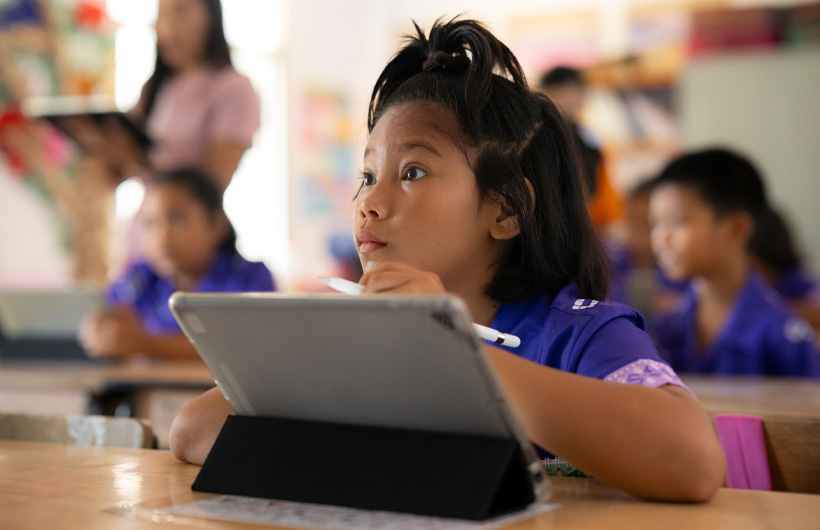 Una niña en su mesa mira con atención hacia el frente de la sala. Usa un iPad con un Apple Pencil.